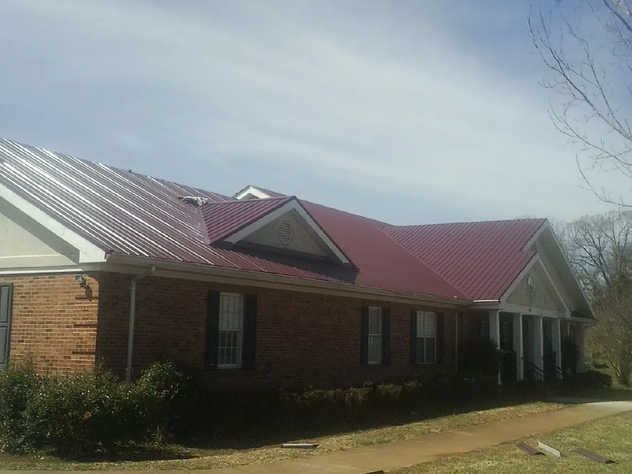Red metal roof with gabled entries on a long brick building, from a Hail Damage Roof Repair job in Lanark