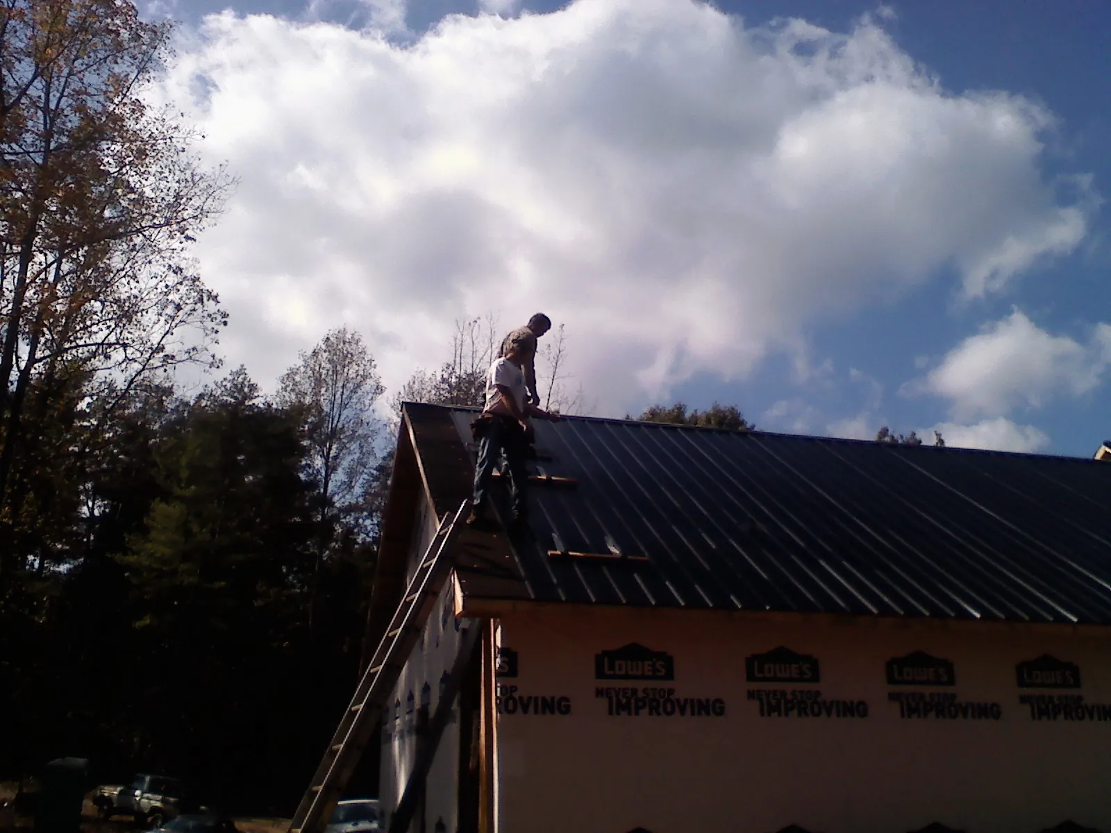Roofer fastening dark metal panels high against a cloudy sky, from a Roof Inspection job in Lanark